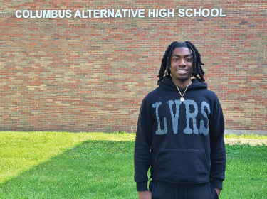 student dressed in black standing in front of brick building